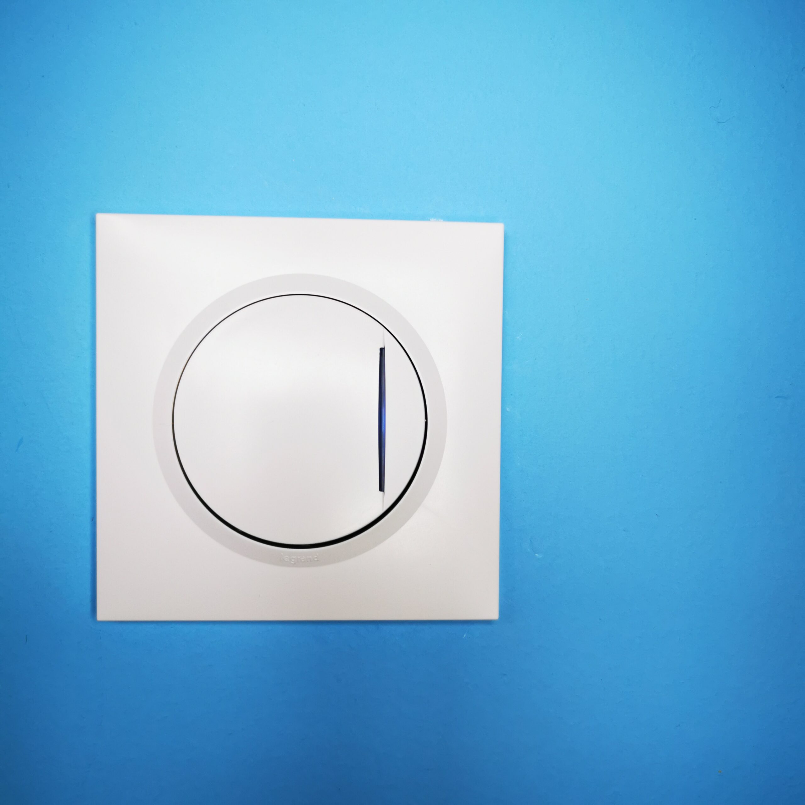 Interrupteur électrique blanc lumineux fixé sur un mur de couleur bleu