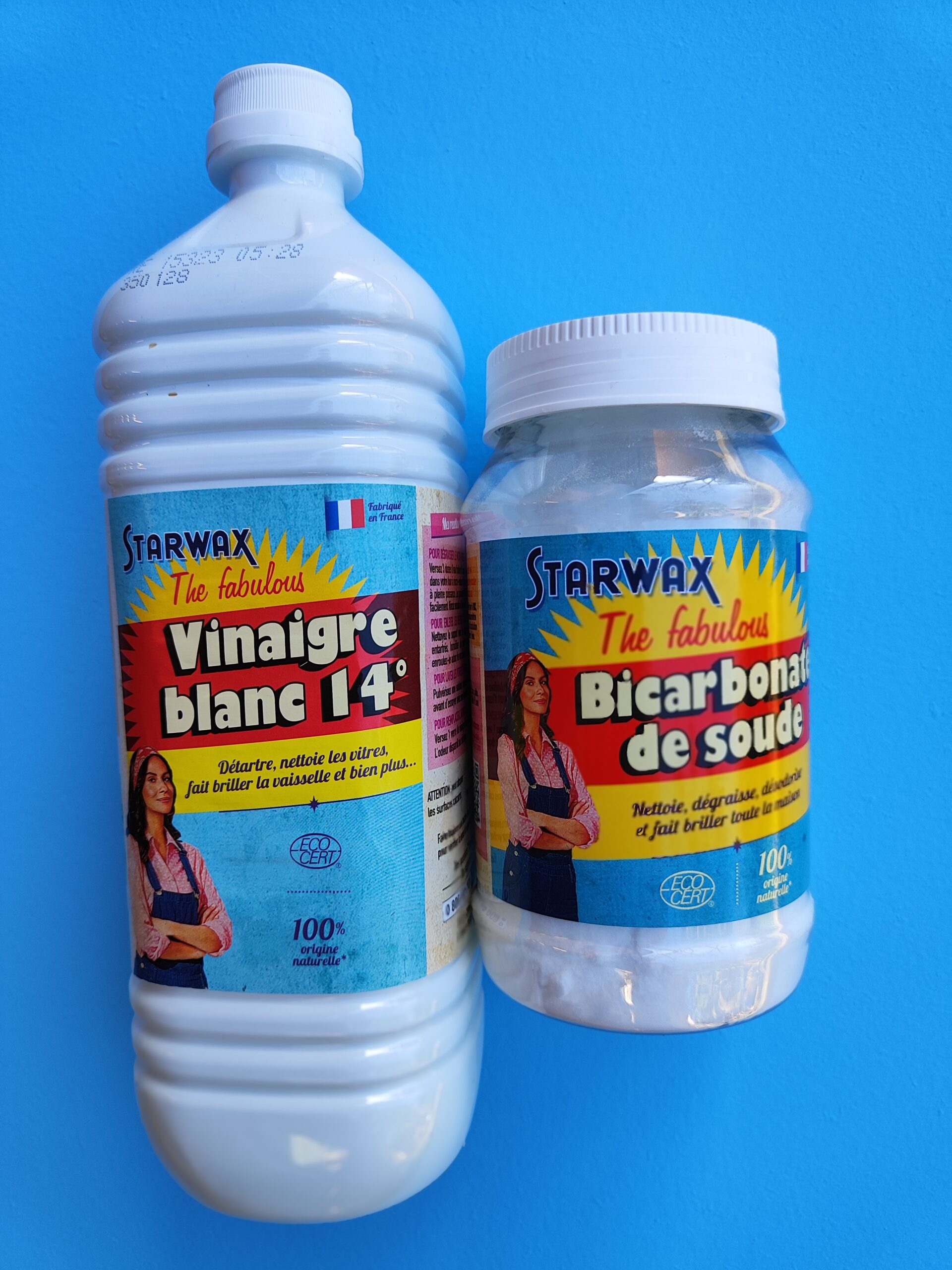 Une bouteille de vinaigre blanc 14 degrés et une boite de bicarbonate de soude sur un fond bleu